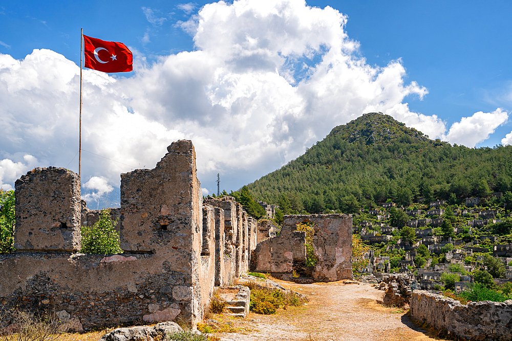 Turkish flag waiving in Kayakoy greek ghost town with abandoned houses in the mountains full of vegetations in Fethiye, Turkey