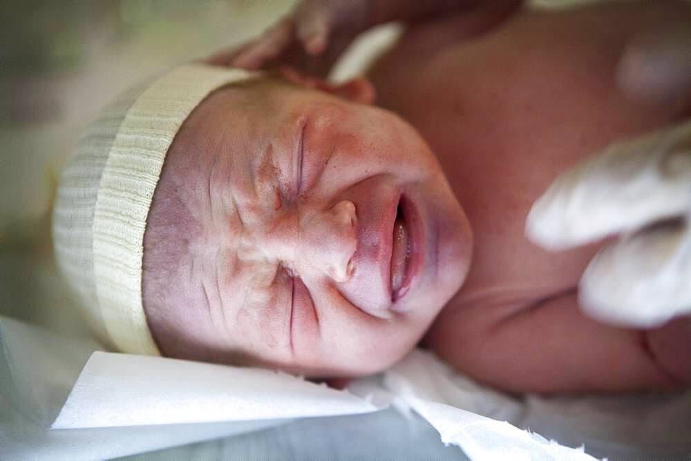 Pediatric nurse is examining a newborn baby a few minutes after the birth.