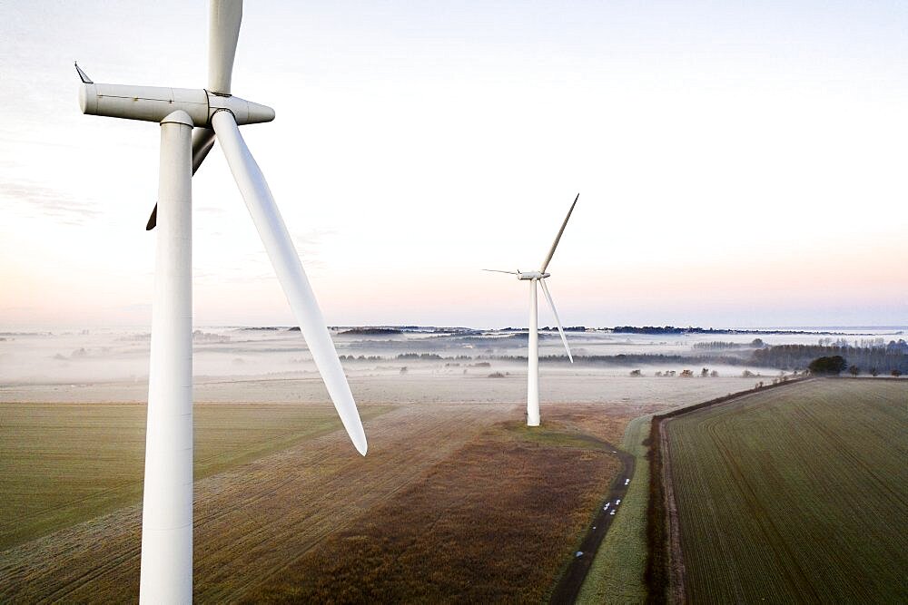 Aerial view of two wind turbines close up at sunrise in the fog in the English countryside