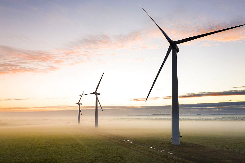 Aerial view of three wind turbines in the early morning fog at sunrise in the English countryside