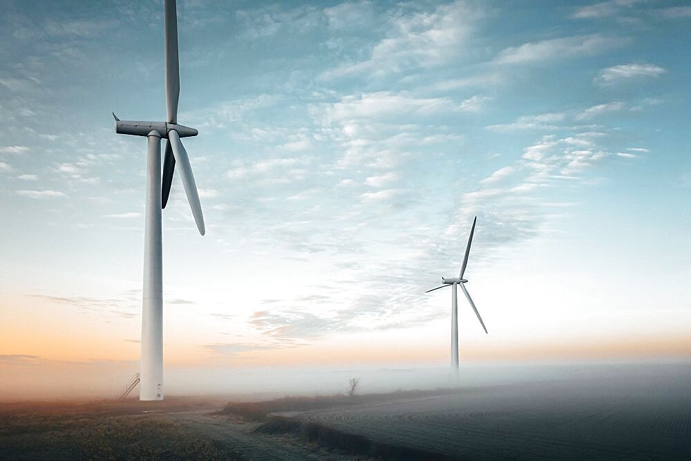 Aerial view of two wind turbines close up at sunrise in the fog in the English countryside