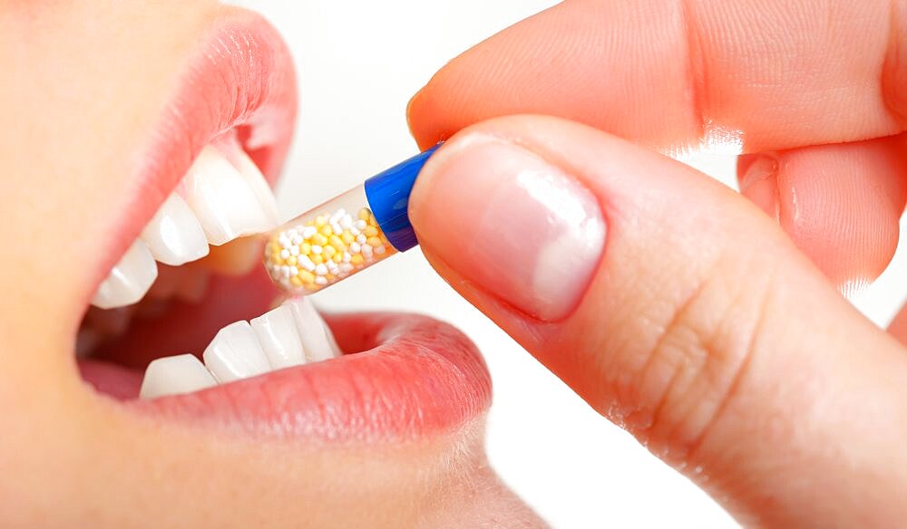 Young woman holding pill by her mouth.