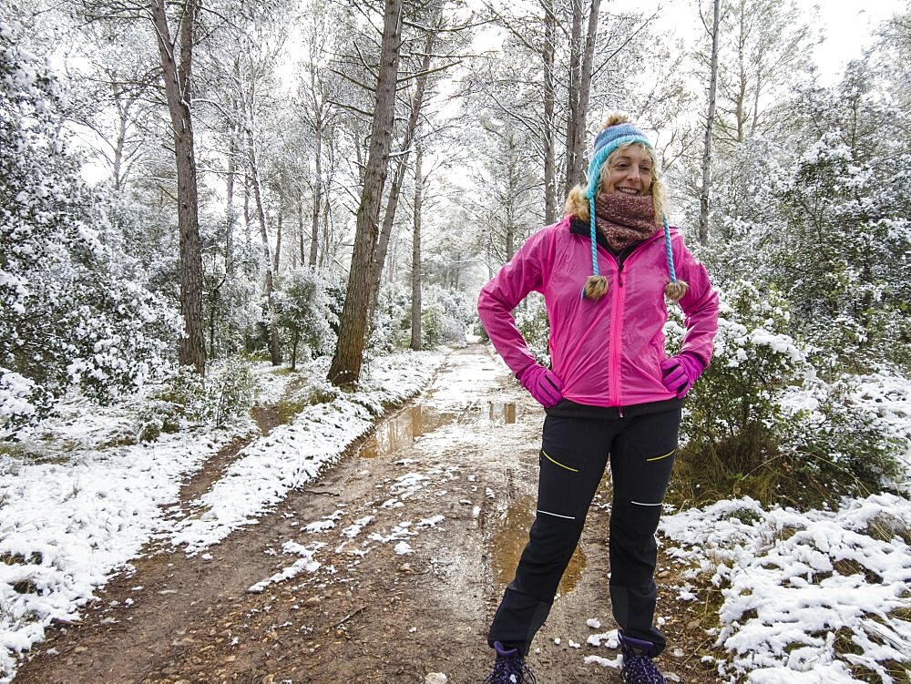 Caucasian young woman with a hat enjoying snow outdoor in a path in a forest area in winter time. Navarre, Spain, Europe.