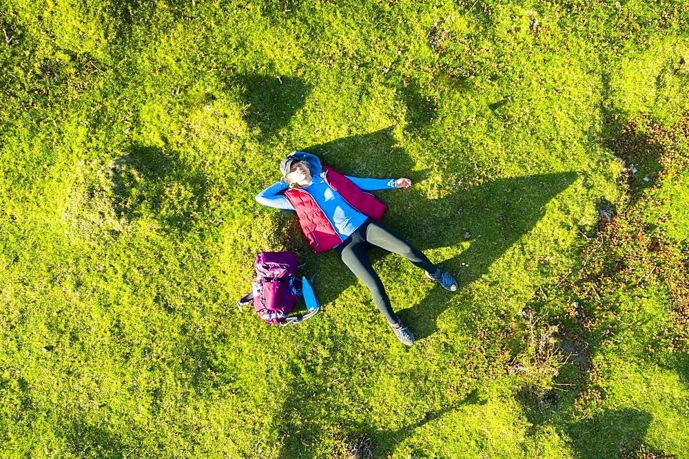 Aerial view of a young woman hiker lying on his back on a meadow. Aralar mountain range. Navarre, Spain, Europe.