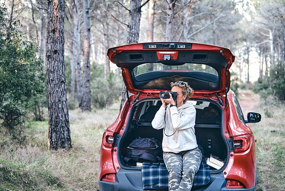 Young adult caucasian woman taking pictures close to a car parked in a forestry path in autumn. Travels concept. Ayegui, Navarre, Spain, Europe.