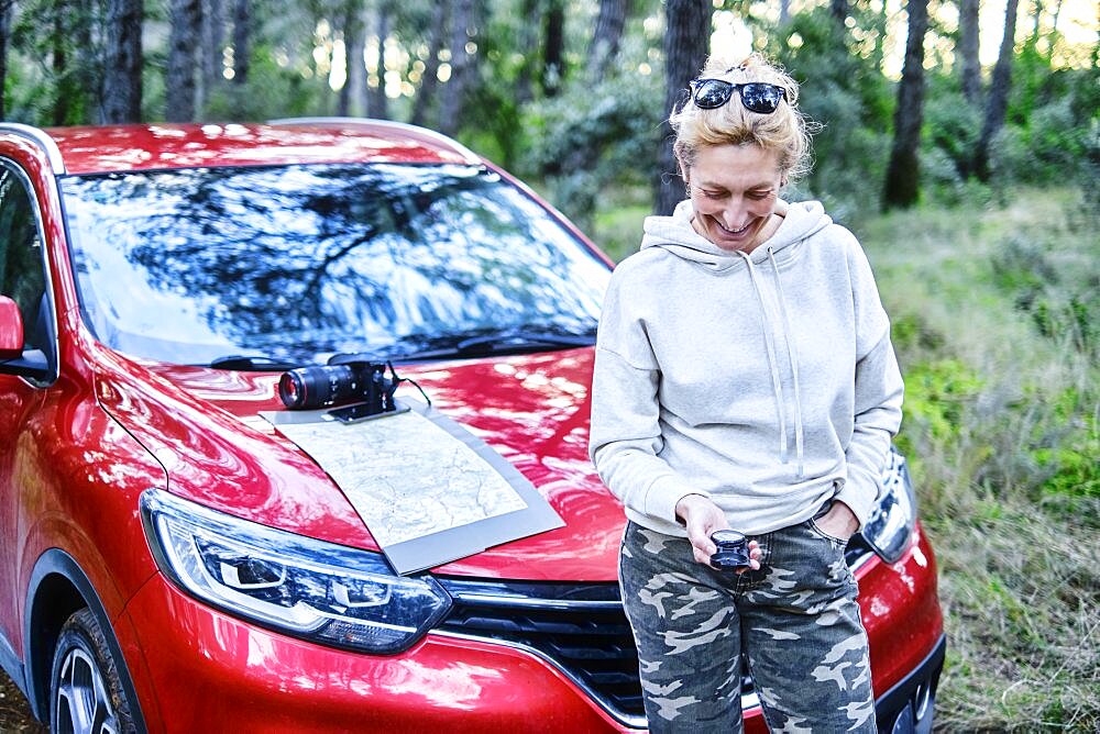 Young adult caucasian woman orienting herself with a map and a compass close to a car parked in a forestry path. Travels concept. Ayegui, Navarre, Spain, Europe.