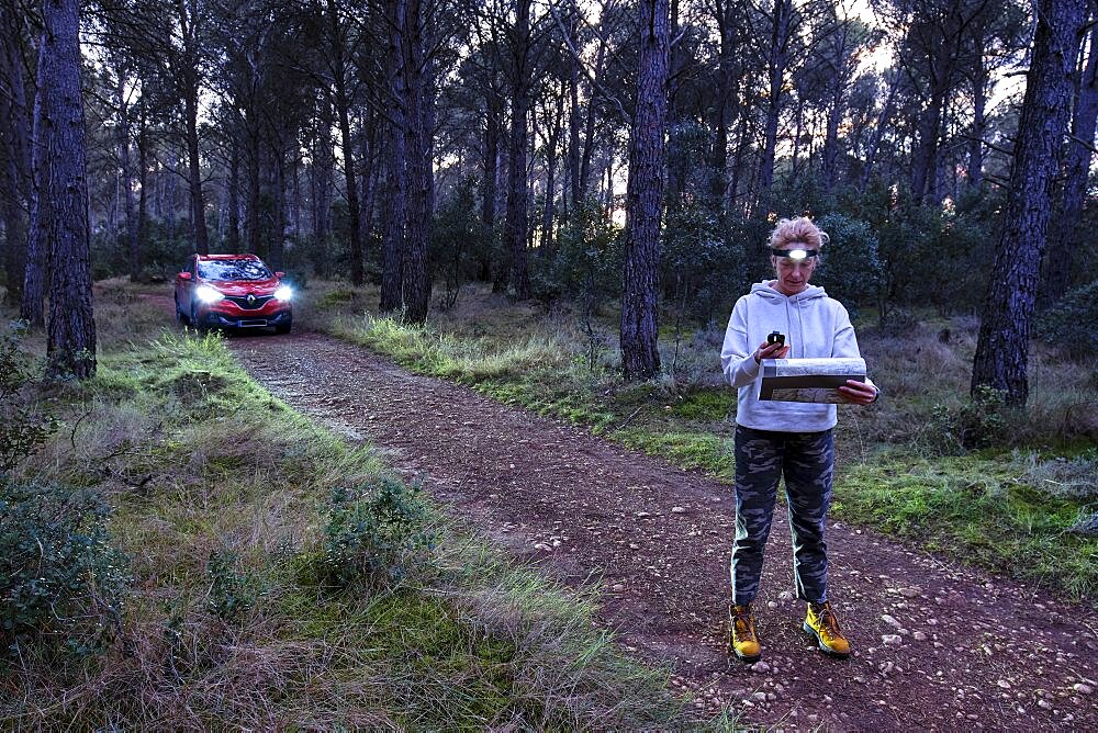 Car and young adult caucasian woman lost in wooded area trying to orient herself at dusk. Travels concept. Ayegui, Navarre, Spain, Europe.