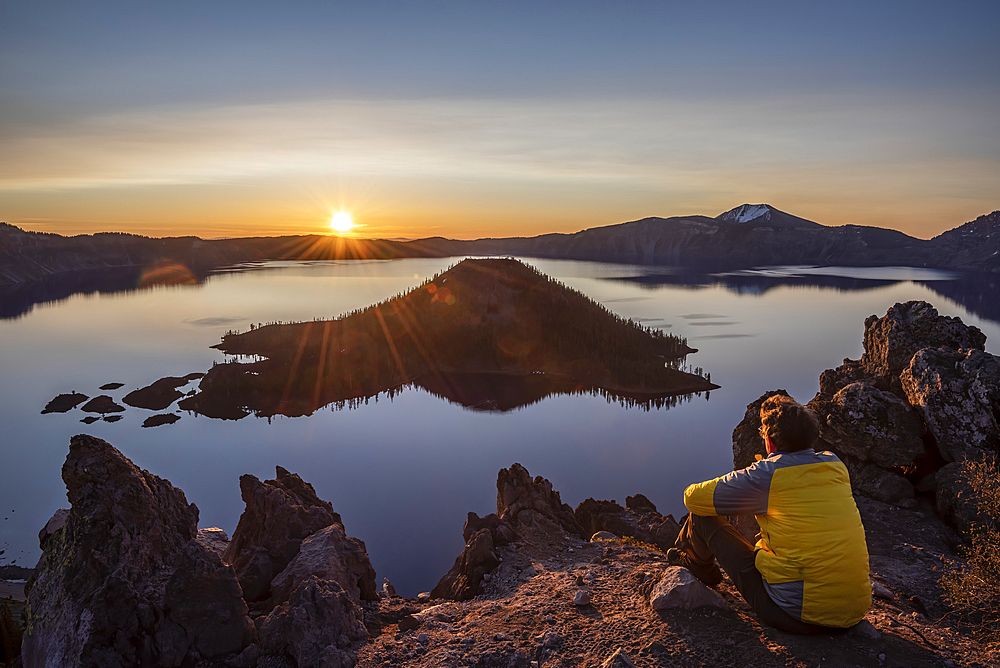 Crater Lake National Park, Oregon: visitor watching sunrise over the lake and Wizard Island, with Mount Scott in the distance.