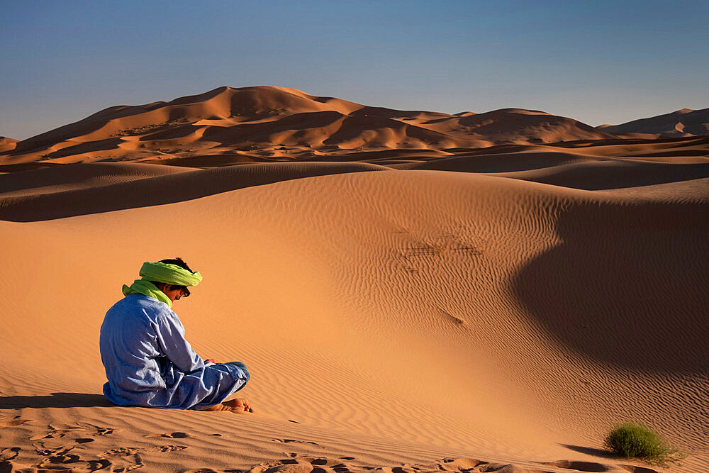 A Berber man in traditional dress sits amongst the Sand Dunes of Erg Chebbi, Sahara Desert, Morocco, North Africa, Africa