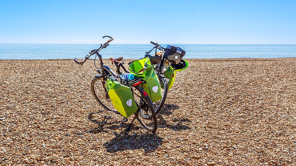 Touring bicycles parked on a sunny pebble beach in East Sussex, England, UK.