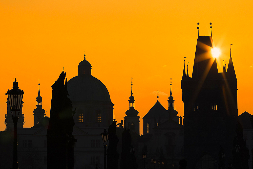 Sun rising above silhouettes of towers and spires at Charles Bridge at sunrise, UNESCO World Heritage Site, Prague, Czechia, Europe