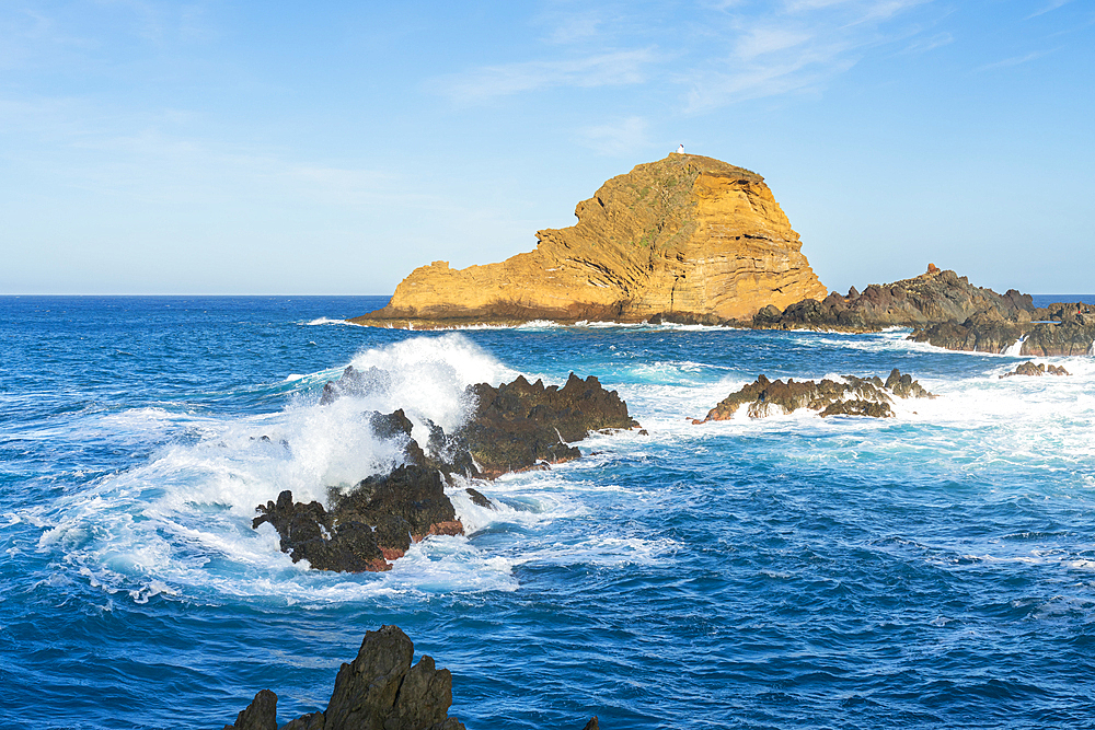 Waves washing rock formation near coast of Porto Moniz and distant view of lighthouse on Ilheu Mole Island, Madeira, Portugal, Atlantic, Europe