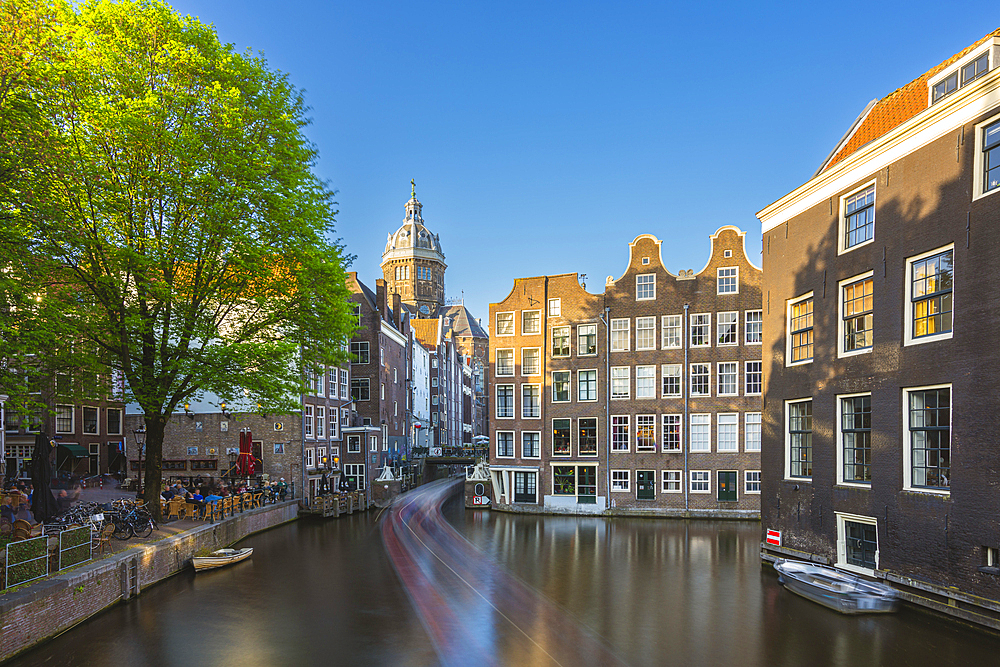 Boat trail on Oudezijds Voorburgwal canal and cupola of Basilica of Saint Nicholas in the background, Amsterdam, The Netherlands, Europe