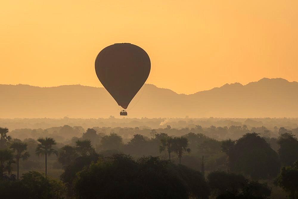 Hot-air balloon at sunrise against mountains, Bagan, Myanmar