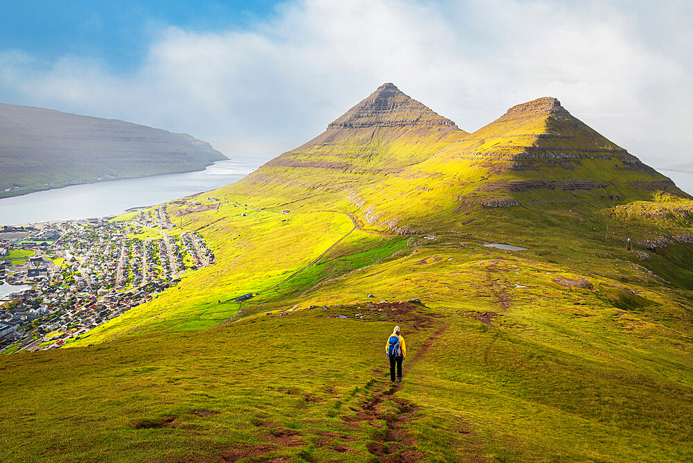 Hiker with yellow jacket walks down the mount Klakker, Klaksvik, Borooy island, Faroe Islands, Denmark, Europe