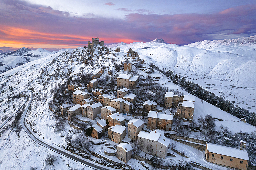 Aerial winter view of the snow covered medieval village of Rocca Calascio with the castle and pink clouds at dusk, Rocca Calascio, Gran Sasso e Monti della Laga National Park, Campo Imperatore, L'Aquila province, Abruzzo region, Italy, Europe