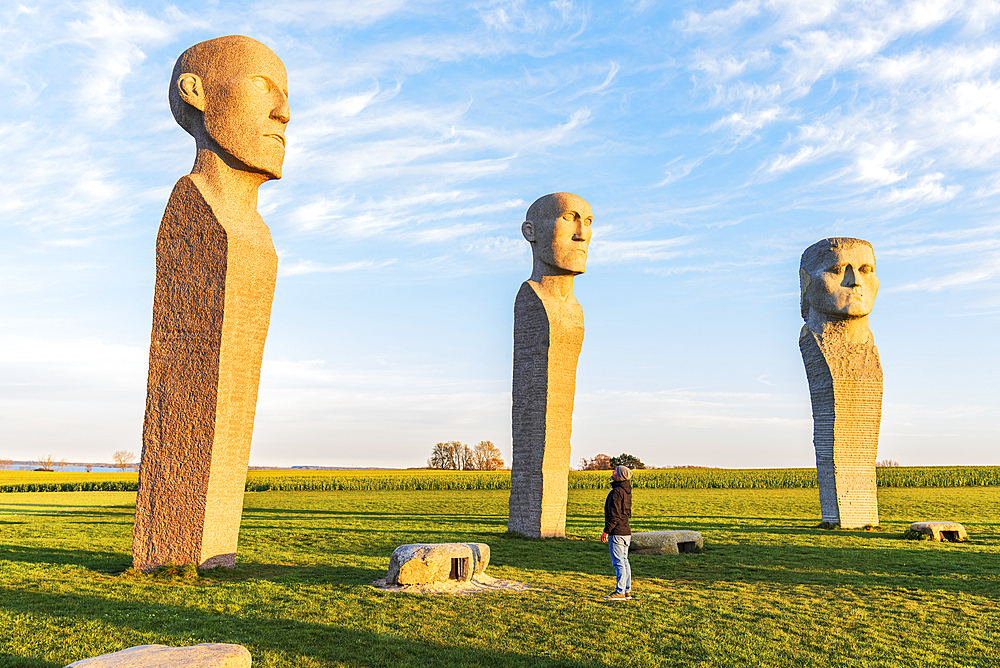 Tourist admiring Dodekalitten statues at sunset, Lolland island, Zealand region, Denmark, Europe