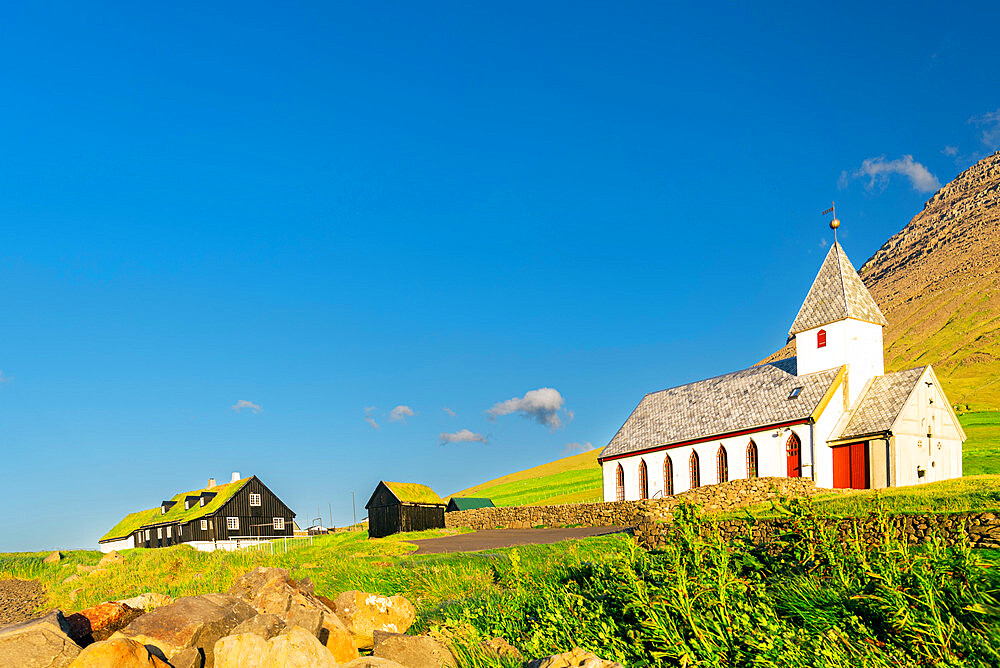 View of the church and grass roof houses among green meadows of Vidareidi, Vidoy island, Faroe Island, Denmark, Europe