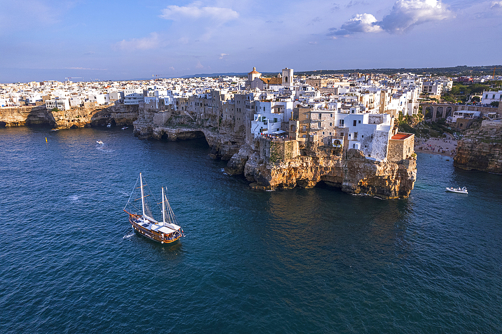 Sail boat anchored in the water off the white village of Polignano a Mare at sunset, Bari province, Adriatic Sea, Mediterranean Sea, Apulia, Italy, Europe