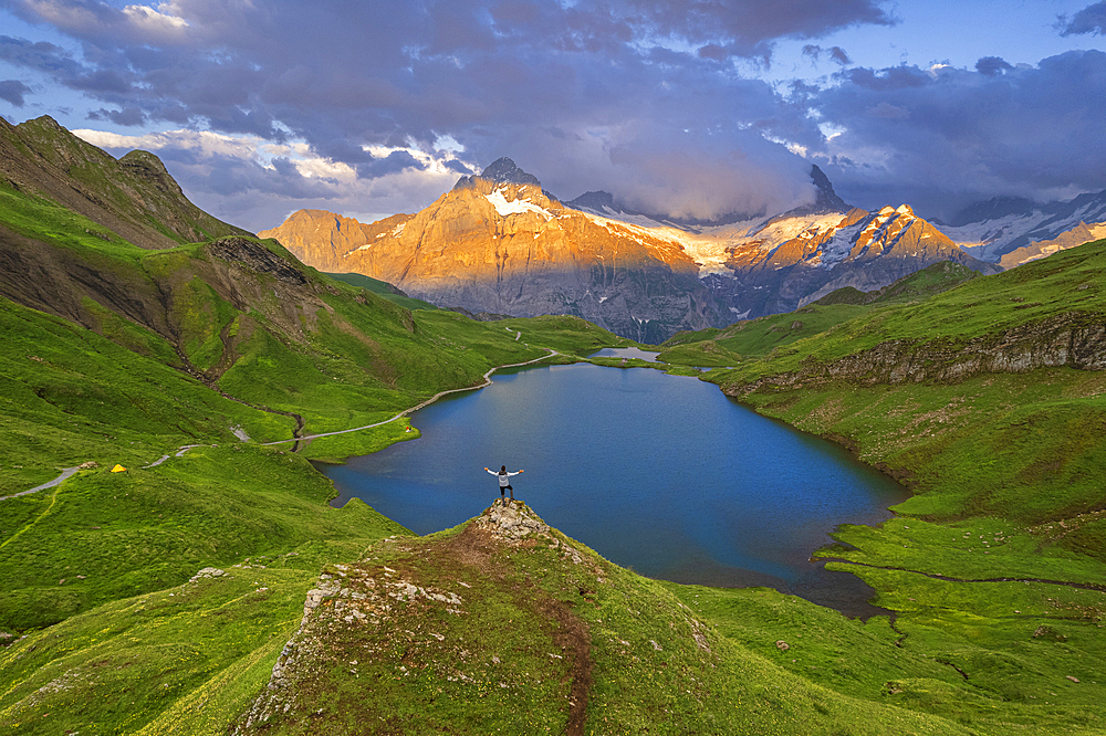 Cheerful hiker overlooking Bachalpseee admiring the sunset over Bernese Oberland mountains, Grindelwald, Bern Canton, Switzerland, Europe