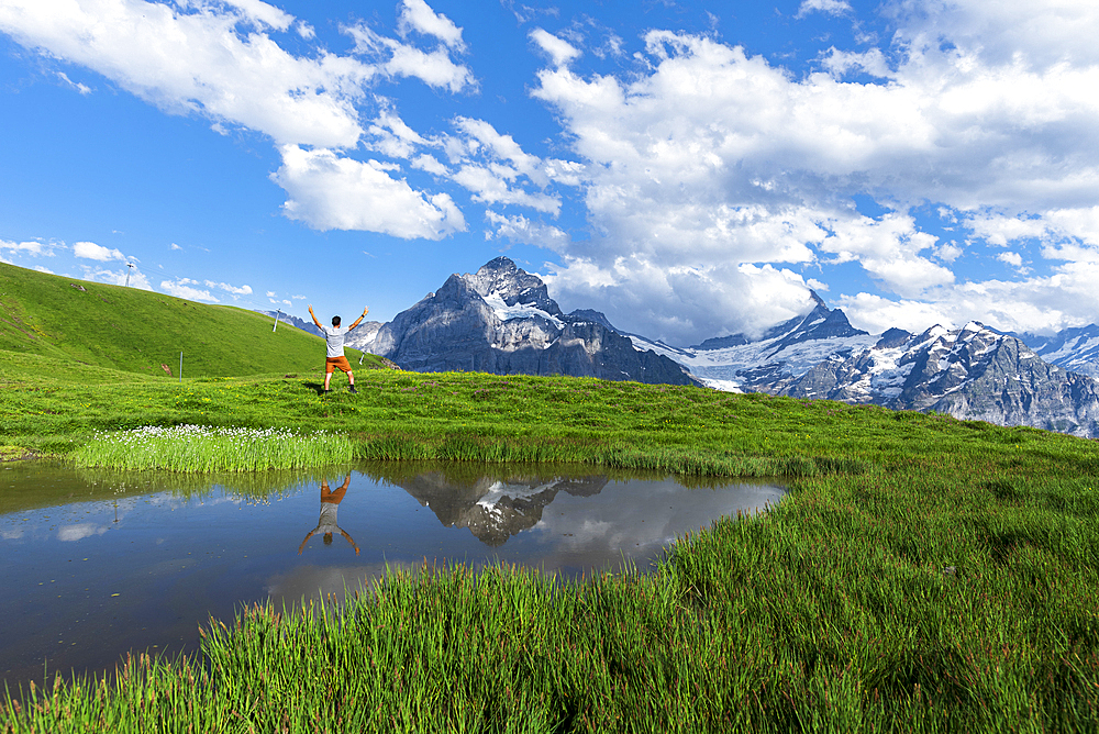 Happy hiker reflecting in the water of a small lake below the Bernese Oberland mountains, Bachalpsee, Grindelwald, Bern canton, Switzerland, Europe