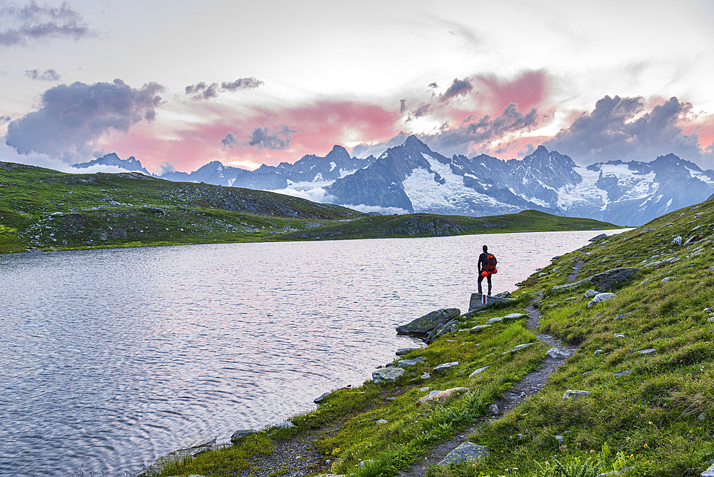 Hiker stands near the shore of Fenetre lake admiring the sunset over the massif of Mount Blanc, Ferret valley, Valais canton, Col du Grand-Saint-Bernard (St. Bernard mountain pass), Switzerland, Europe