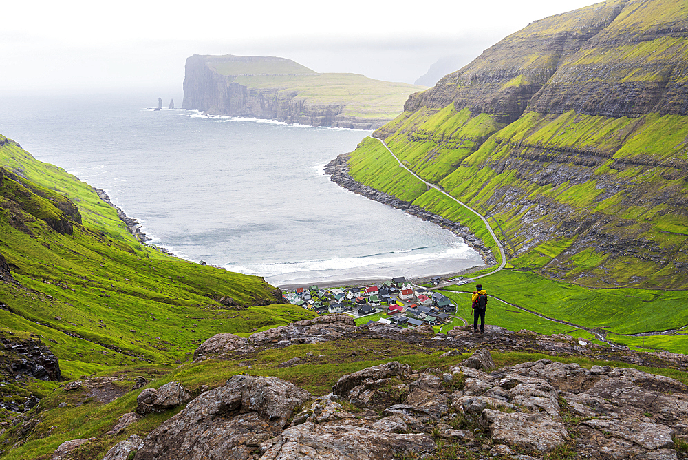 One man on top of a rock admiring the village of Tjornuvik in the misty weather, Sunda municipality, Streymoy island, Faroe islands, Denmark, Europe