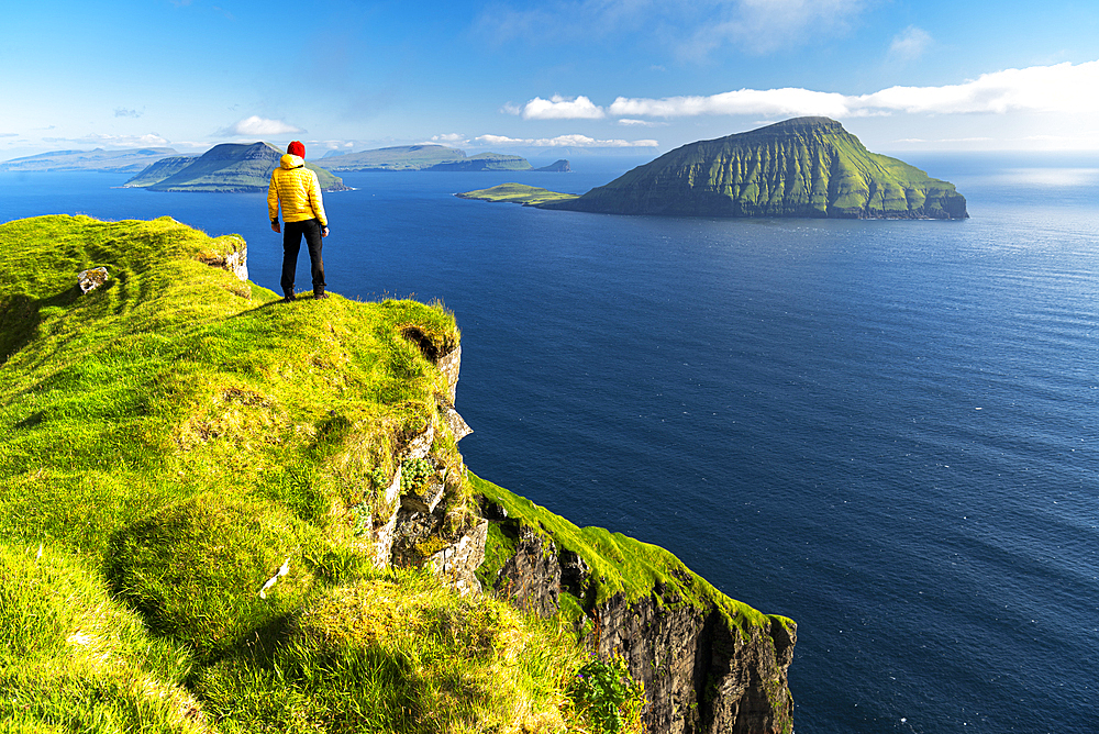 Hiker stands on top of a cliff admiring the rugged view, Nordradalur, Streymoy island, Faroe islands, Denmark, Europe