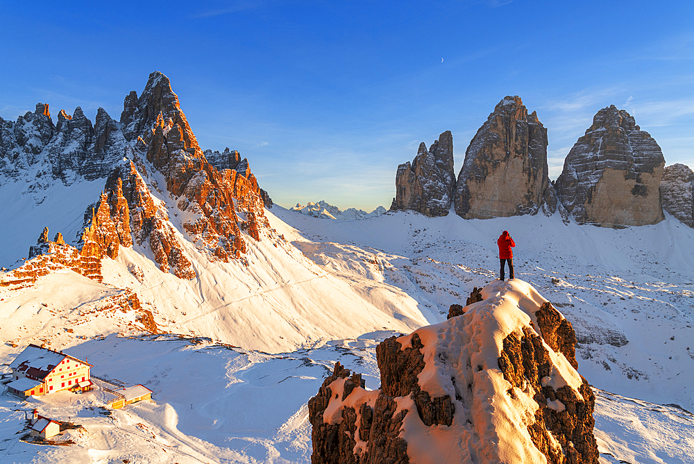 Rear view of a hiker admiring Tre Cime di Lavaredo (Lavaredo Peaks) (Drei Zinnen) from the top of a giant rock, winter view, Sesto (Sexten), Dolomites, South Tyrol, Italy, Europe