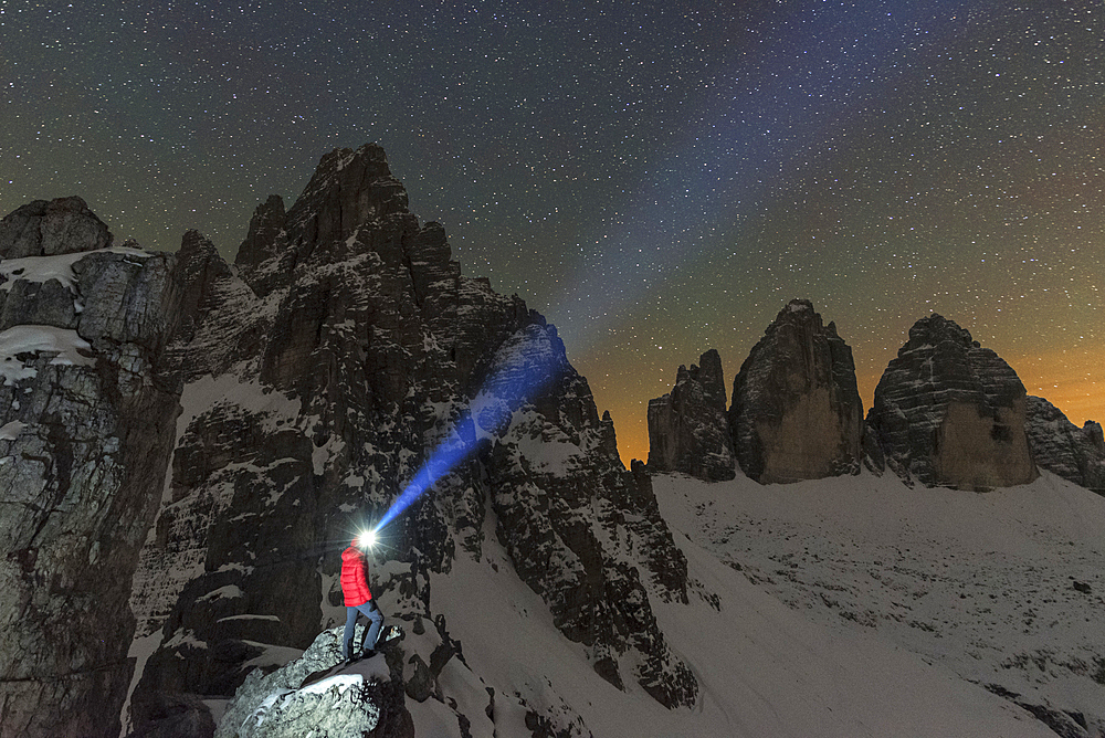 Man with head torch illuminates the starry sky over the snowy Paterno mountain and Tre Cime di Lavaredo (Lavaredo peaks), Sesto (Sexten), Dolomites, South Tyrol, Italy, Europe