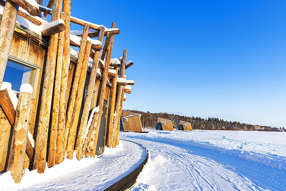 Architectural structure of Arctic Bath hotel made of logs on frozen Lule River with cutting-edge chalets in the background, Harads, Norrbotten, Swedish Lapland, Sweden, Scandinavia, Europe