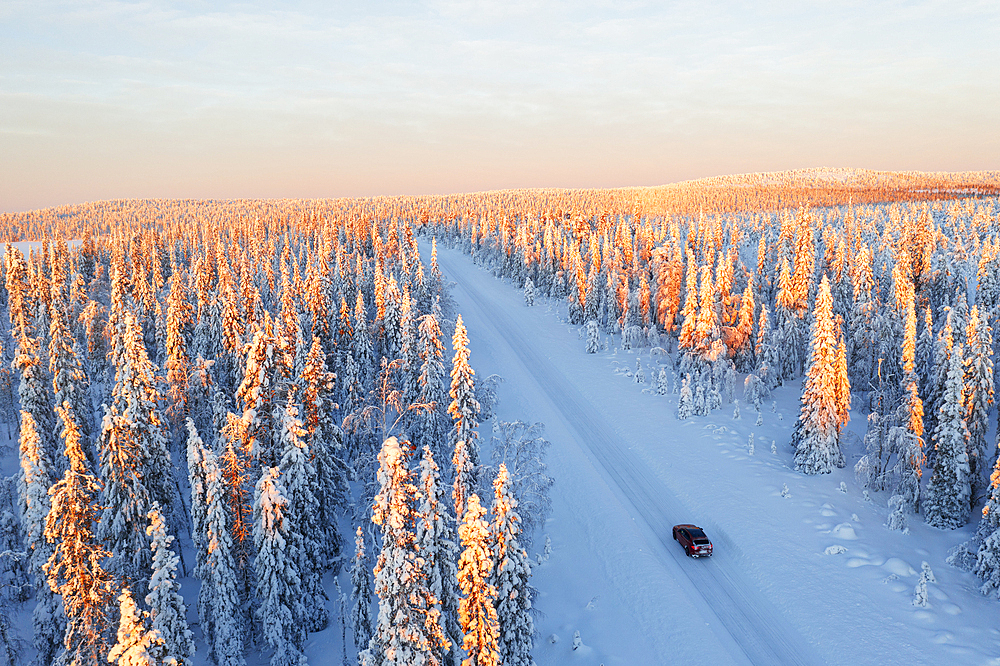 View from a drone of a car travelling an icy road among pine tree wood at sunrise, Swedish Lapland, Sweden, Scandinavia, Europe