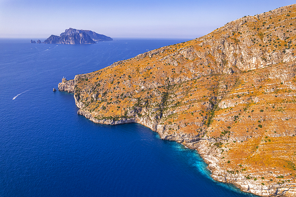 Aerial view of a rocky coast facing the blue water of the Tyrrhenian Sea with the island of Capri in the background, Amalfi Coast, Naples province, Campania region, South of Italy, Italy, Europe