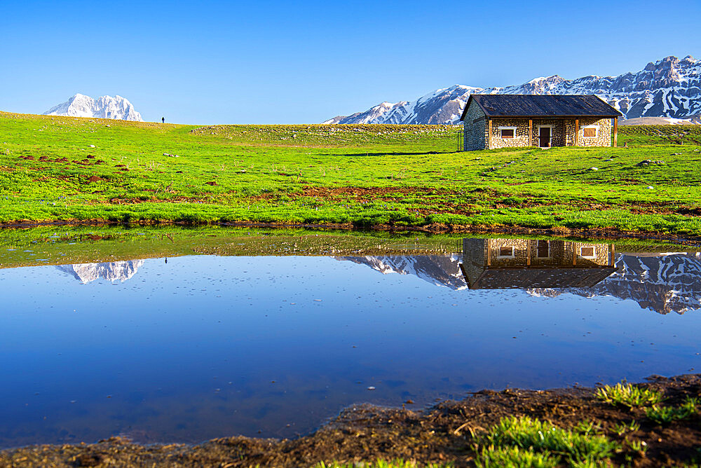 Reflections of the peak of Gran Sasso and a mountain hut among meadows, Campo Imperatore, Abruzzo, Apennines, Italy, Europe