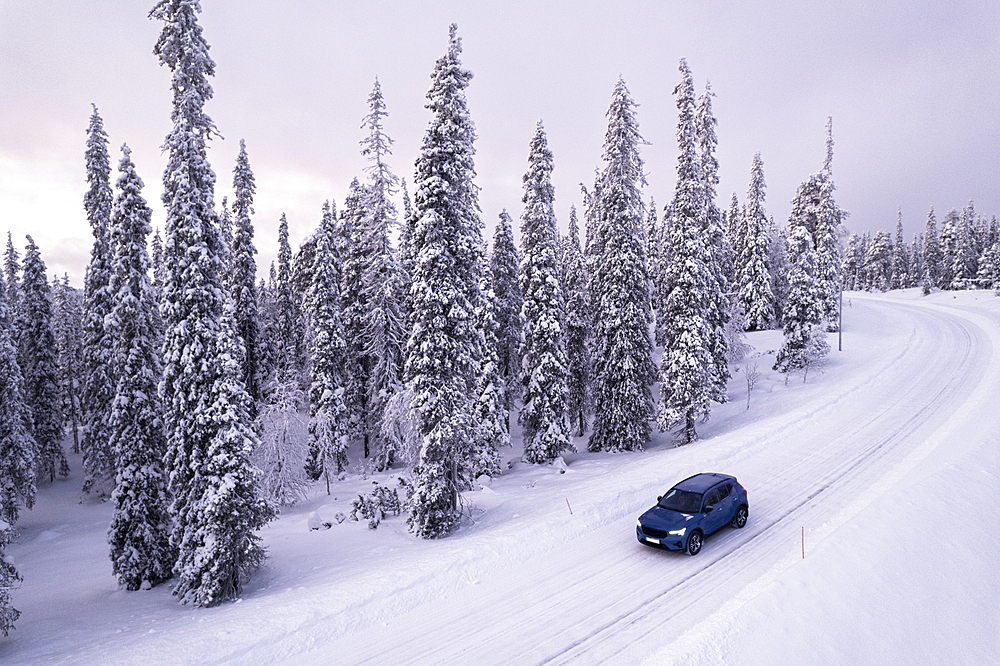 Aerial shot of a car driving across snow-capped forest in the Arctic landscape of Finnish Lapland, Pallas-Yllastunturi National Park, Muonio, Finland, Scandinavia, Europe