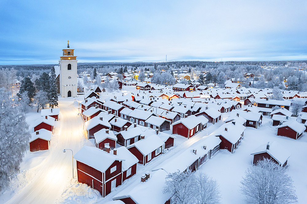 Aerial winter view of the old illuminated Gammelstad covered with snow with red cottages around the church, Gammelstad Church Town, UNESCO World Heritage Site, Lulea, Norrbotten, Swedish Lapland, Sweden, Scandinavia, Europe