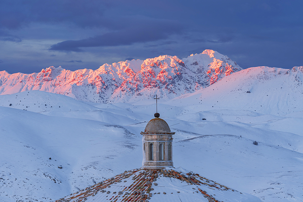 Close-up view of the roof of the church of Santa Maria della Pieta with snow covered mountains of Gran Sasso lit at sunset, Rocca Calascio, Gran Sasso e Monti della Laga National Park, Campo Imperatore, L'Aquila province, Abruzzo, Italy, Europe