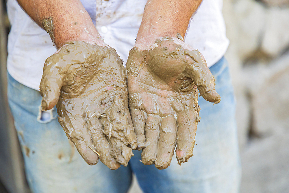 Mavzoley Rudaki, Sughd Province, Tajikistan. The muddy hands of a worker applying mud plaster to a traditional stone house.