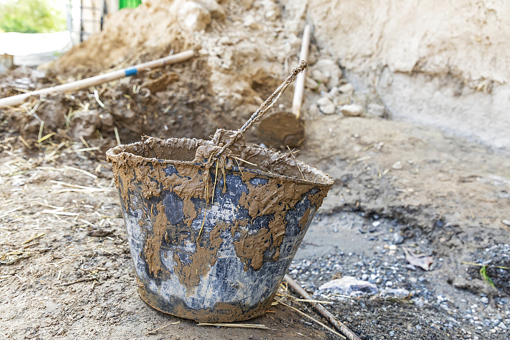 Mavzoley Rudaki, Sughd Province, Tajikistan. A muddy bucket being used to apply mud plaster to a traditional stone house.