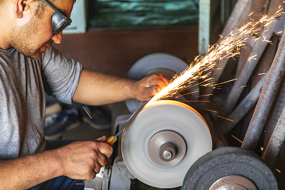 Istaravshan, Sughd Province, Tajikistan. August 19, 2021. Worker grinding metal tools at a blacksmith shop. Editorial Use Only