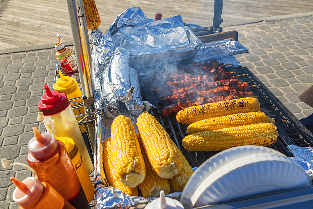 Coney Island, Brooklyn, New York City, New York, USA. Meat kebabs and corn on the cob at a sidewalk food stand.