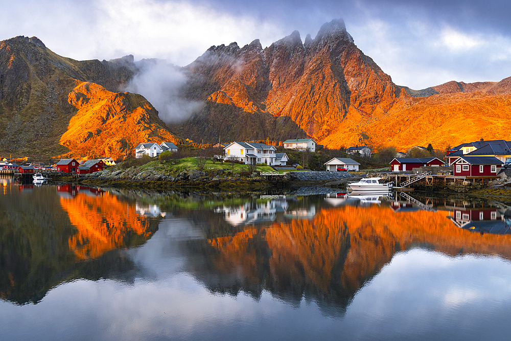 Reflections of houses and mountains in the water at Ballstad village during sunrise, Vestvagoy, Nordland, Lofoten Islands, Norway, Europe