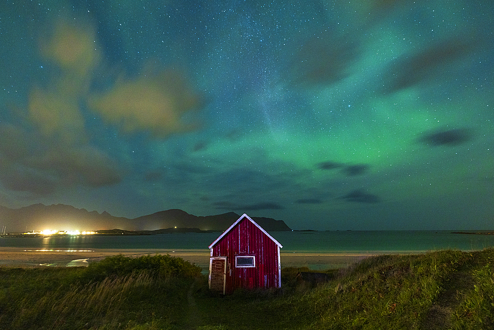 Northern Lights (Aurora Borealis) fill the sky over the red cabin close to Ramberg beach during an autumn night, Lofoten Islands, Nordland, Norway, Scandinavia, Europe