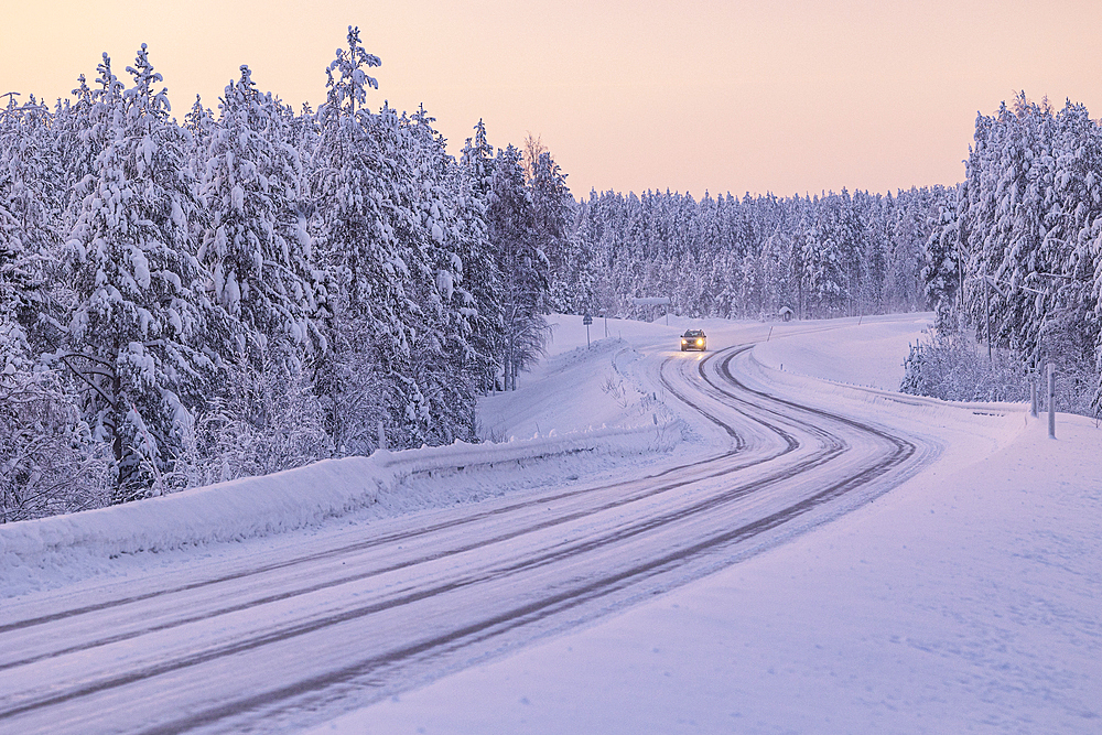 A car driving along a snow-covered road along the Finnish Lapland forest during a winter blue hour, Muonio, Finland, Europe