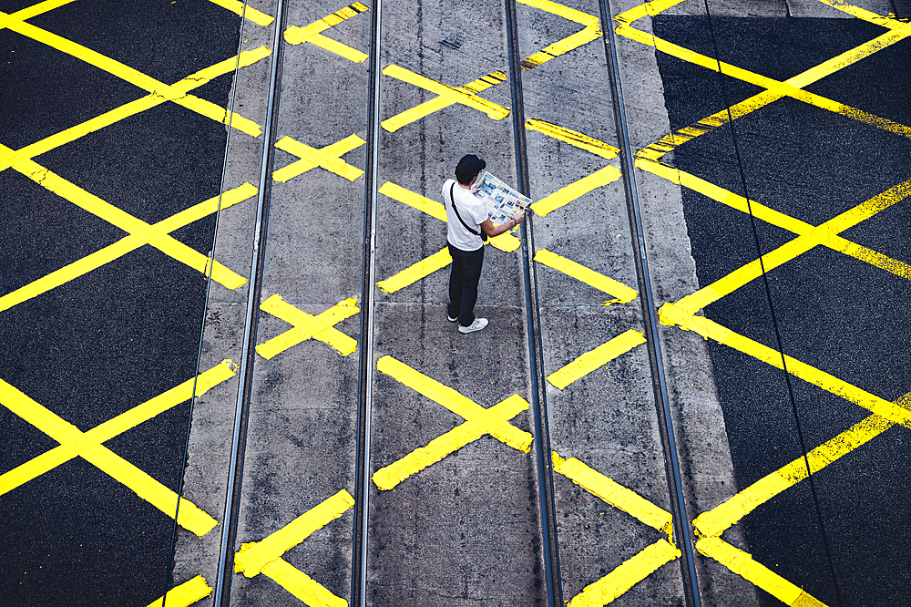 A tourist reads the newspaper on the pedestrian crossing, Central District, Hong Kong, China, Asia