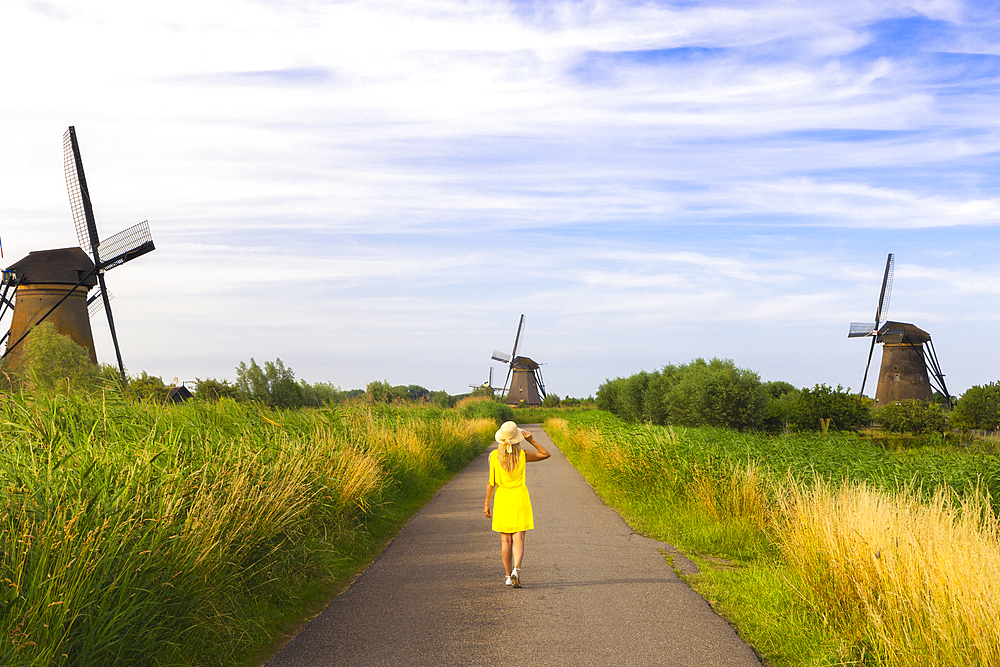 A tourist walks in the midst of Unesco Windmills of Kinderdijk during sunset, Molenlanden, Alblasserdam, South Holland, Netherlands, Northern Europe