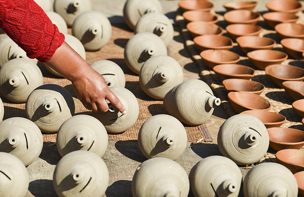 A craftswoman shows off the traditional clay pots she left to dry in the sun, Bhaktapur, Nepal, Asia