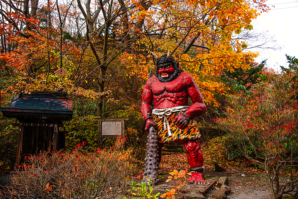 Standing red demon statue with a big club in autmn forest, Noboribetsu, Hokkaido, Japan, Asia