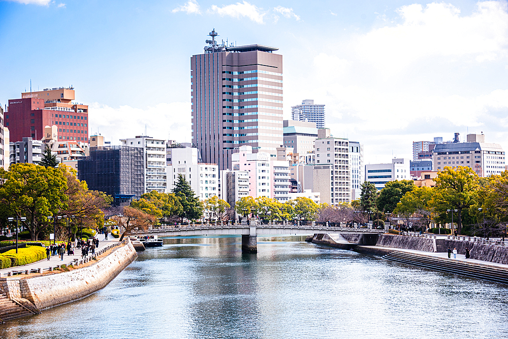 Motoyasu Bridge and Hiroshima cityscape on a bright day with reflections on the river and people walking along the promenade
