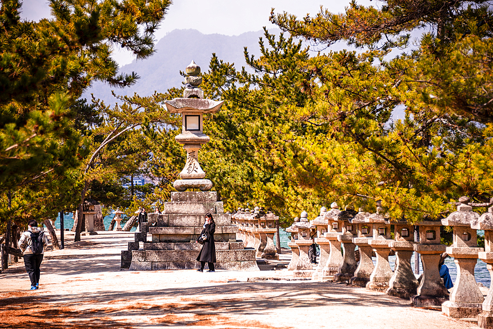 Tourists Walking Along Stone Lantern Path at Momijidani Park Near Itsukushima Shrine, Miyajima Island, Japan